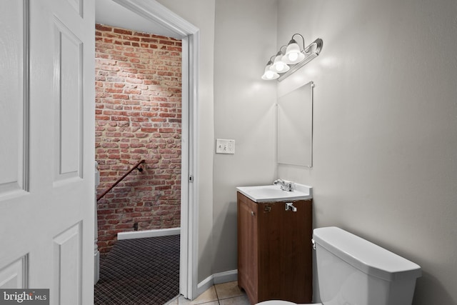 half bathroom with baseboards, toilet, brick wall, tile patterned flooring, and vanity