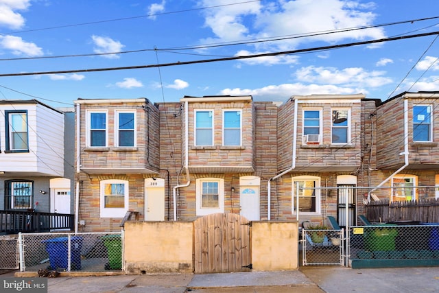 townhome / multi-family property featuring stone siding, a fenced front yard, and a gate