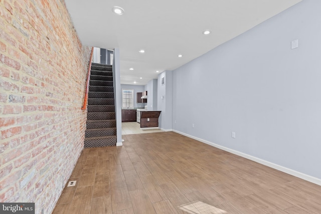 unfurnished living room with light wood finished floors, brick wall, stairs, and baseboards