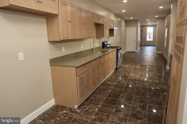 kitchen featuring baseboards, stainless steel range with gas cooktop, dark stone counters, a sink, and a baseboard heating unit