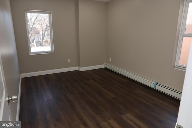 empty room featuring dark wood-type flooring, a baseboard heating unit, and baseboards