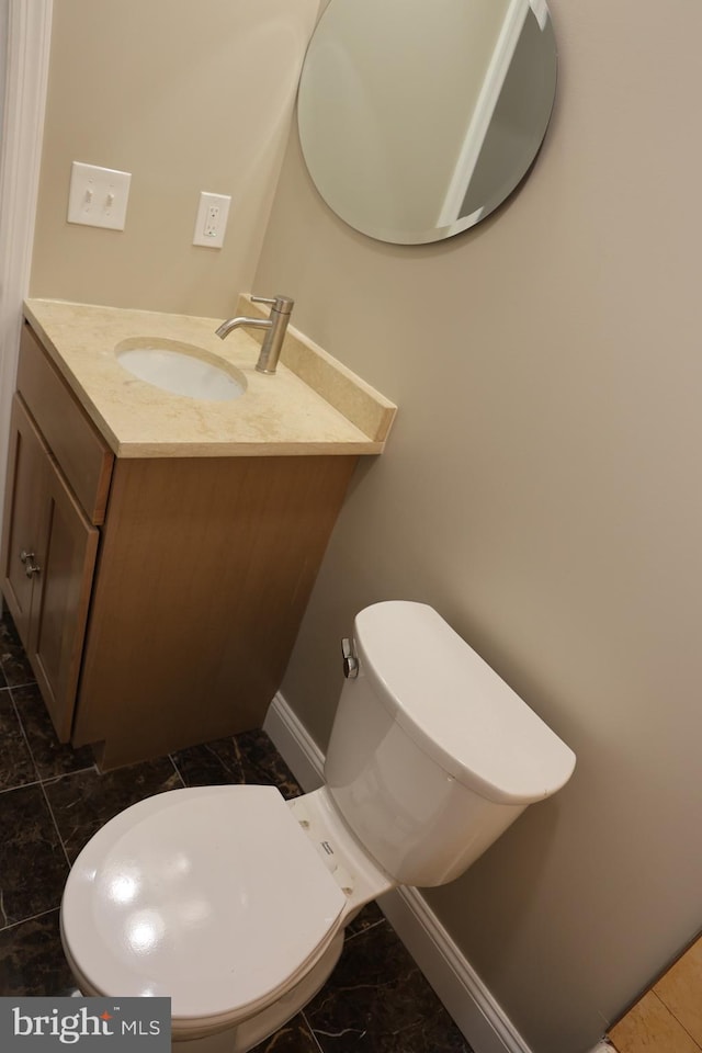 half bath with vanity, toilet, baseboards, and marble finish floor