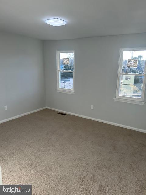 empty room featuring baseboards, visible vents, plenty of natural light, and carpet flooring