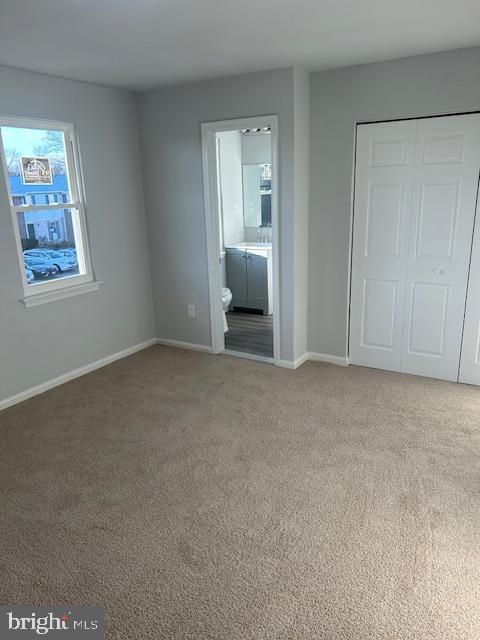 unfurnished bedroom with baseboards, ensuite bathroom, a closet, and light colored carpet