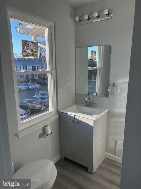 bathroom with toilet, wood finished floors, visible vents, vanity, and baseboards