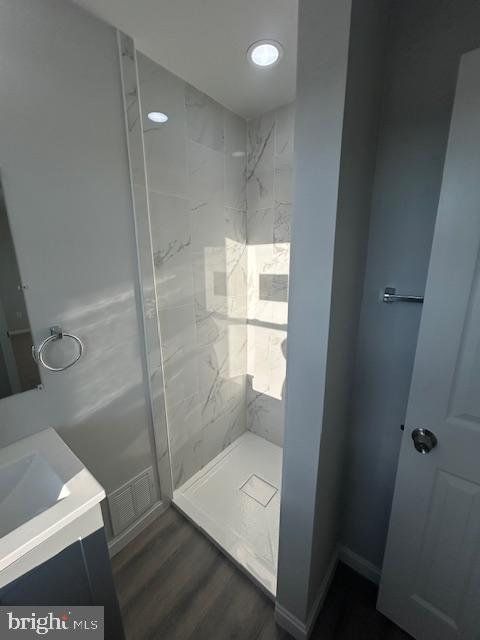 full bathroom featuring vanity, wood finished floors, a shower stall, and visible vents