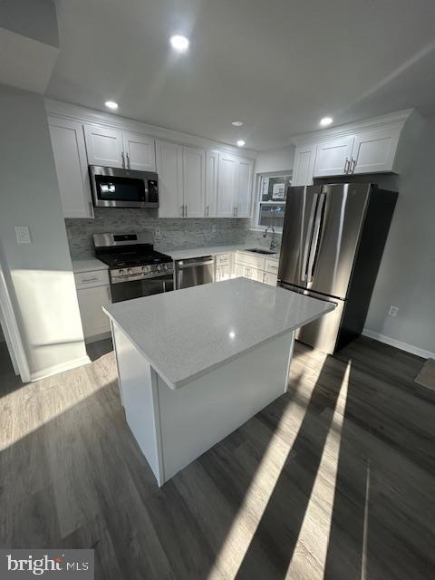 kitchen featuring tasteful backsplash, white cabinets, appliances with stainless steel finishes, dark wood-type flooring, and a center island