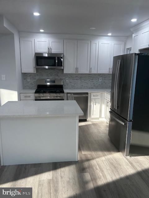 kitchen featuring light stone counters, tasteful backsplash, light wood-style flooring, appliances with stainless steel finishes, and white cabinetry