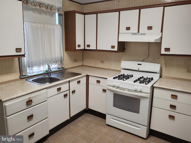 kitchen featuring under cabinet range hood, light countertops, gas range gas stove, and white cabinets