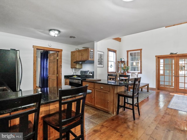 kitchen with brown cabinetry, dark countertops, a breakfast bar, stainless steel appliances, and french doors