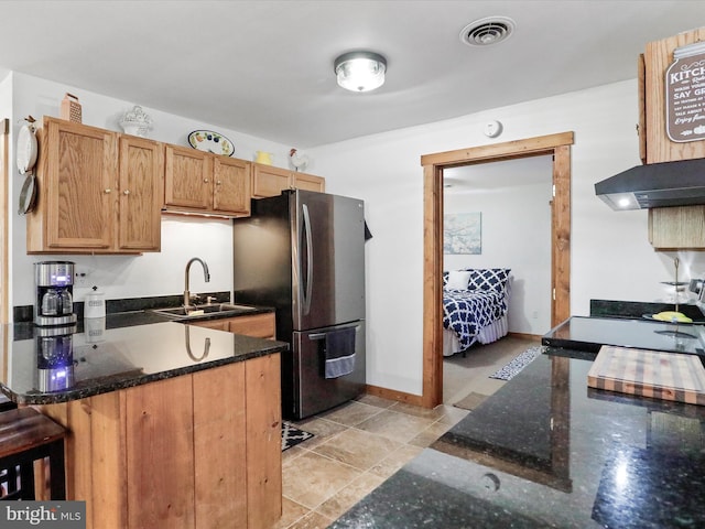 kitchen with visible vents, freestanding refrigerator, a sink, dark stone counters, and extractor fan