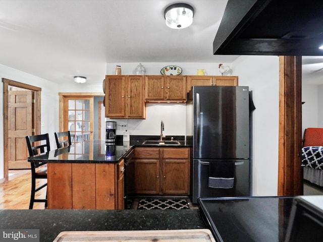 kitchen featuring brown cabinetry, freestanding refrigerator, a sink, a peninsula, and a kitchen bar