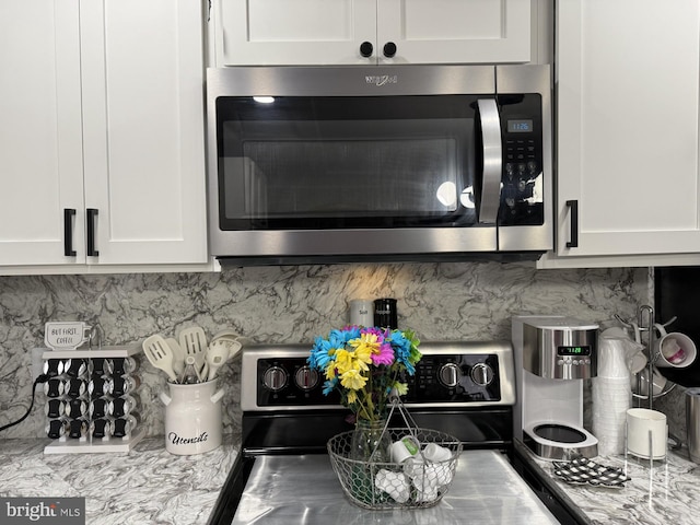 kitchen featuring electric range, stainless steel microwave, white cabinetry, and decorative backsplash