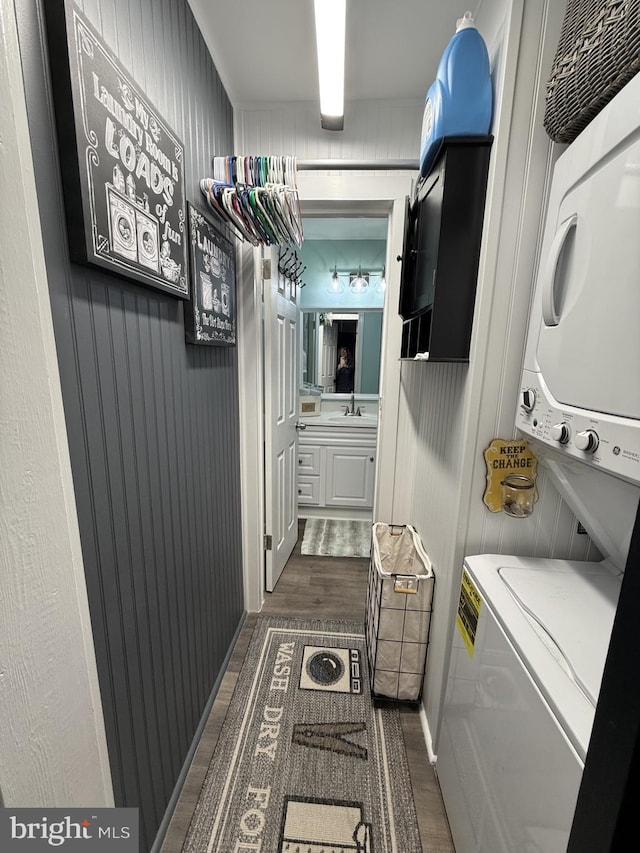 washroom featuring stacked washer and dryer, laundry area, dark wood finished floors, and a sink