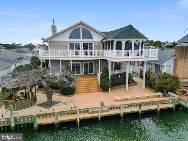 rear view of house featuring stairway, a deck with water view, and a chimney