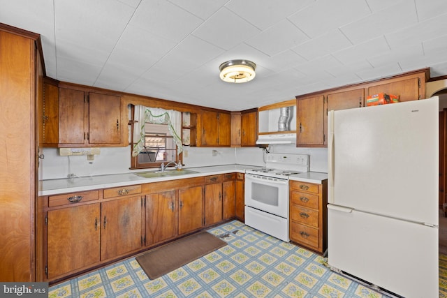 kitchen with white appliances, under cabinet range hood, light countertops, and a sink