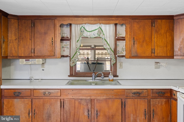 kitchen featuring light countertops, a sink, range, and brown cabinets