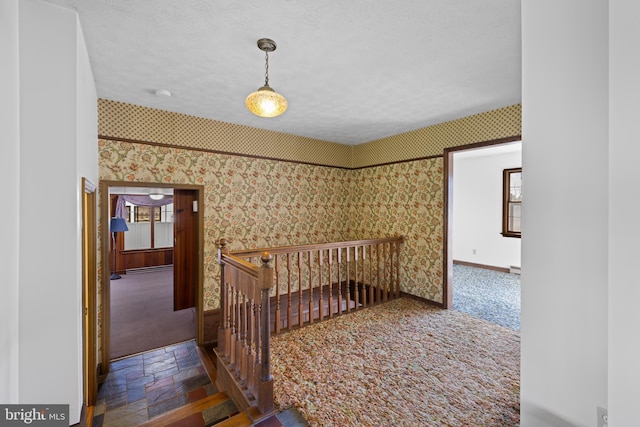 interior space with carpet flooring, a textured ceiling, baseboards, and wallpapered walls