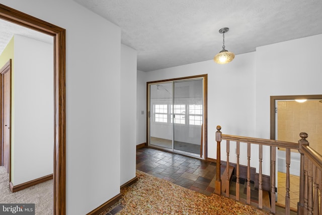 corridor featuring an upstairs landing, stone tile floors, a textured ceiling, and baseboards