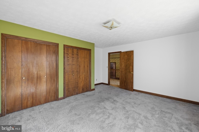 unfurnished bedroom with carpet, a textured ceiling, baseboards, and multiple closets