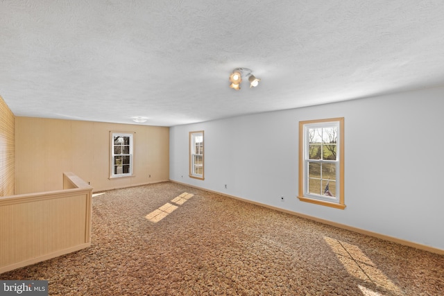 spare room featuring a wealth of natural light, carpet flooring, a textured ceiling, and baseboards