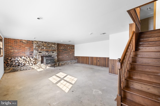 unfurnished living room featuring wooden walls, visible vents, a wainscoted wall, stairway, and concrete flooring