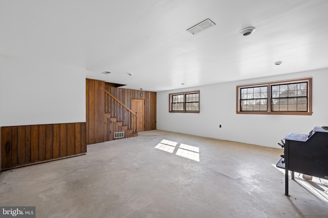 unfurnished living room with concrete floors, stairs, wooden walls, and visible vents