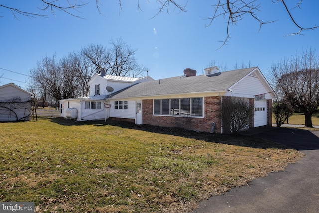 view of front facade featuring brick siding, a chimney, aphalt driveway, an attached garage, and a front yard