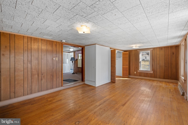 unfurnished room featuring hardwood / wood-style flooring, a baseboard radiator, baseboards, and wood walls