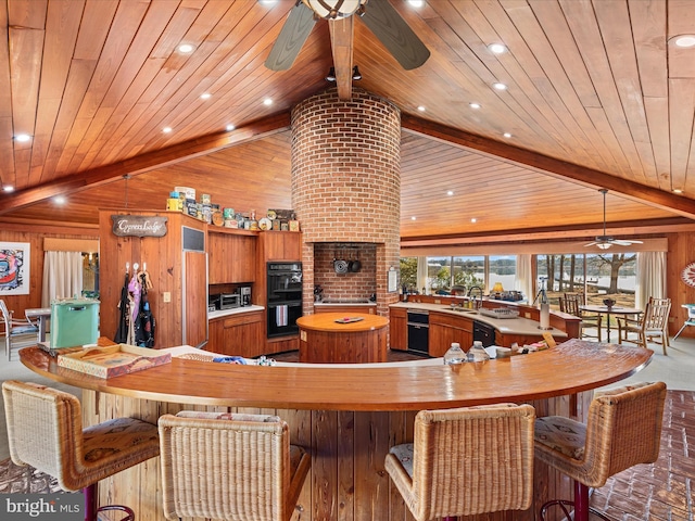 kitchen featuring black appliances, vaulted ceiling with beams, brown cabinets, and a spacious island