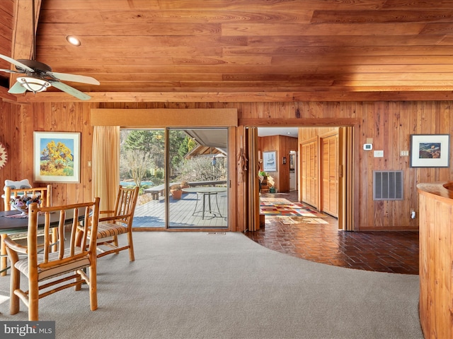 carpeted dining space featuring visible vents, wooden walls, wooden ceiling, and a ceiling fan