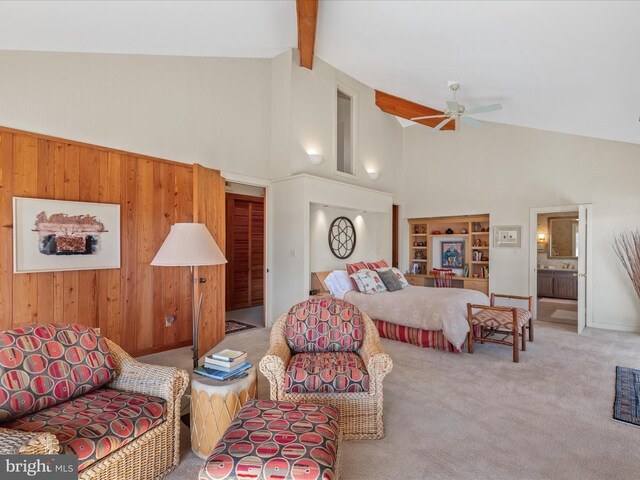 carpeted bedroom featuring wooden walls, high vaulted ceiling, beam ceiling, ceiling fan, and connected bathroom