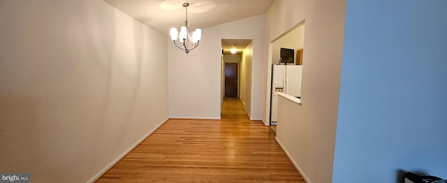 hallway featuring light wood-type flooring, a notable chandelier, vaulted ceiling, and baseboards