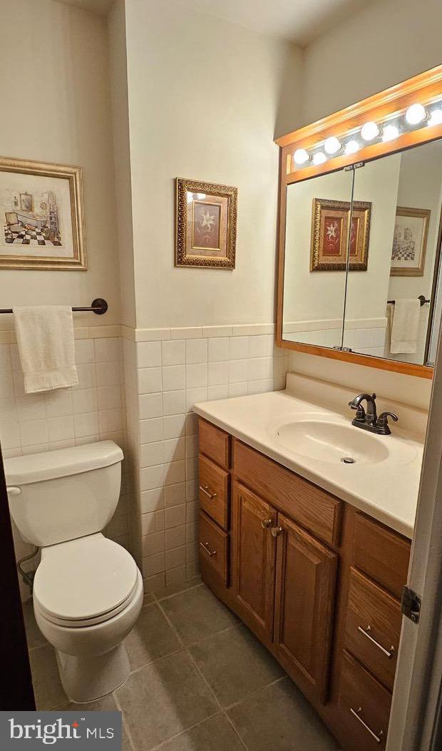 half bathroom with tile walls, toilet, wainscoting, vanity, and tile patterned floors