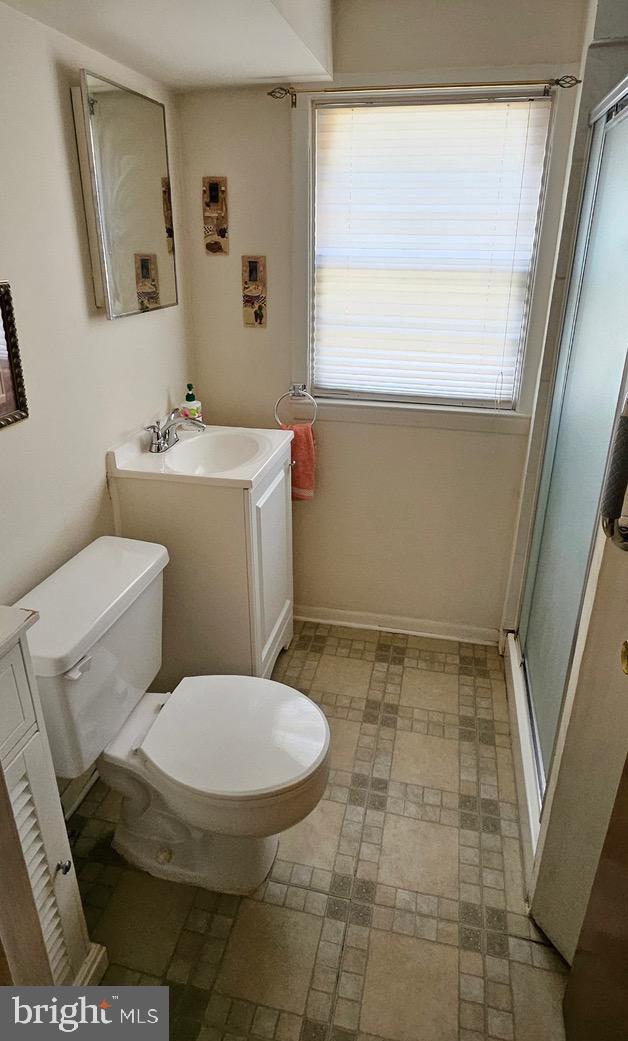 bathroom with toilet, a stall shower, vanity, and baseboards