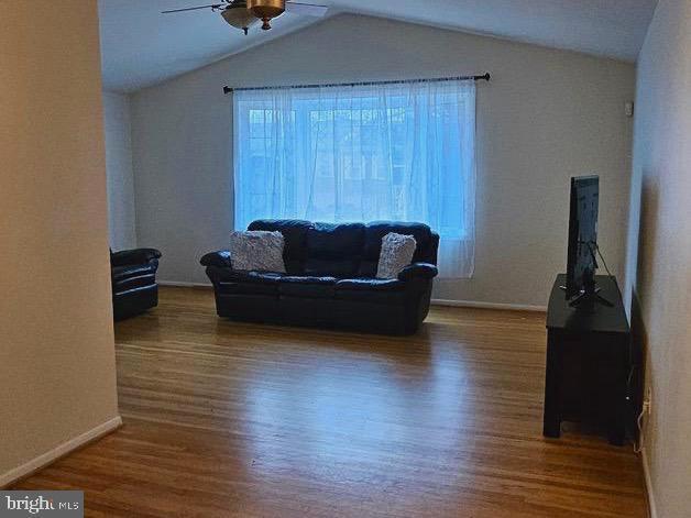 living area with baseboards, a ceiling fan, vaulted ceiling, and wood finished floors