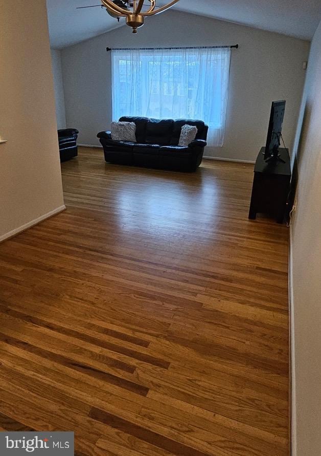 unfurnished living room featuring a notable chandelier, vaulted ceiling, and wood finished floors