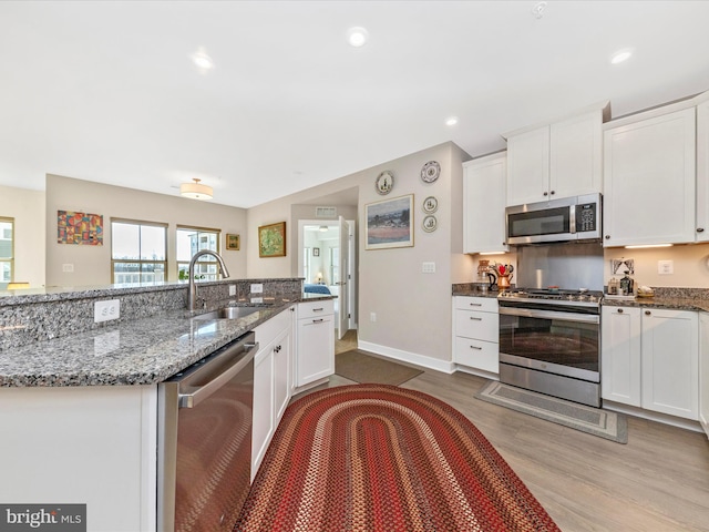 kitchen with wood finished floors, white cabinets, stainless steel appliances, and a sink