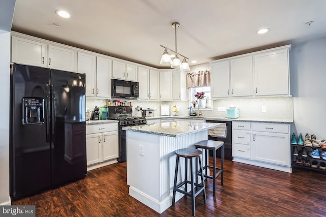 kitchen featuring dark wood-type flooring, a center island, white cabinetry, light stone countertops, and black appliances