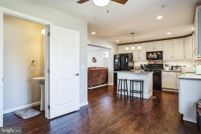 kitchen with stone countertops, decorative backsplash, a kitchen island, dark wood-style flooring, and black appliances