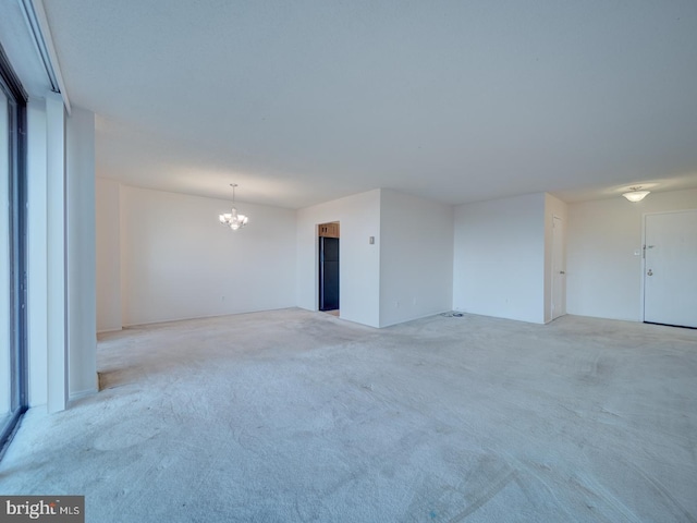 empty room with light colored carpet and an inviting chandelier