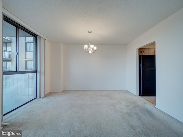 spare room featuring a textured ceiling, an inviting chandelier, and light colored carpet