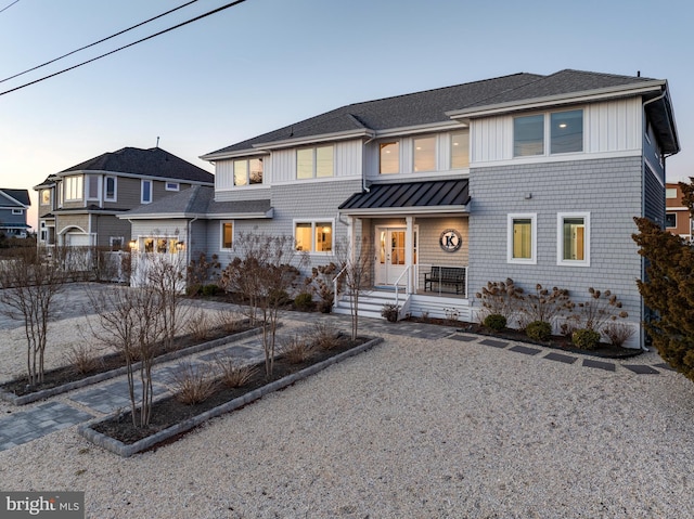 shingle-style home featuring a shingled roof, a standing seam roof, fence, metal roof, and driveway