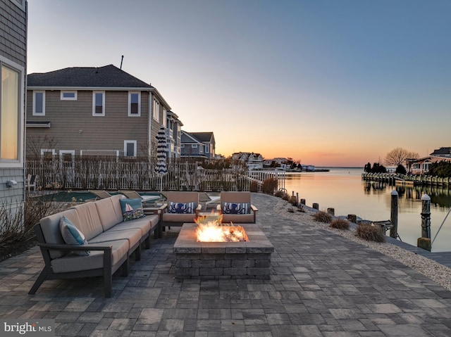 patio terrace at dusk with a water view, an outdoor living space with a fire pit, and fence