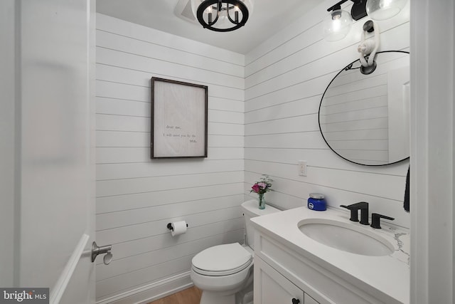 bathroom featuring vanity, toilet, and wooden walls