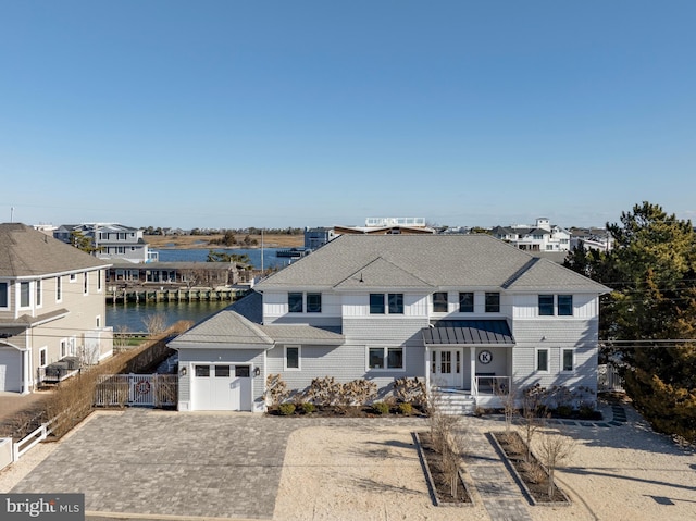 view of front of property with driveway, a garage, roof with shingles, a water view, and fence