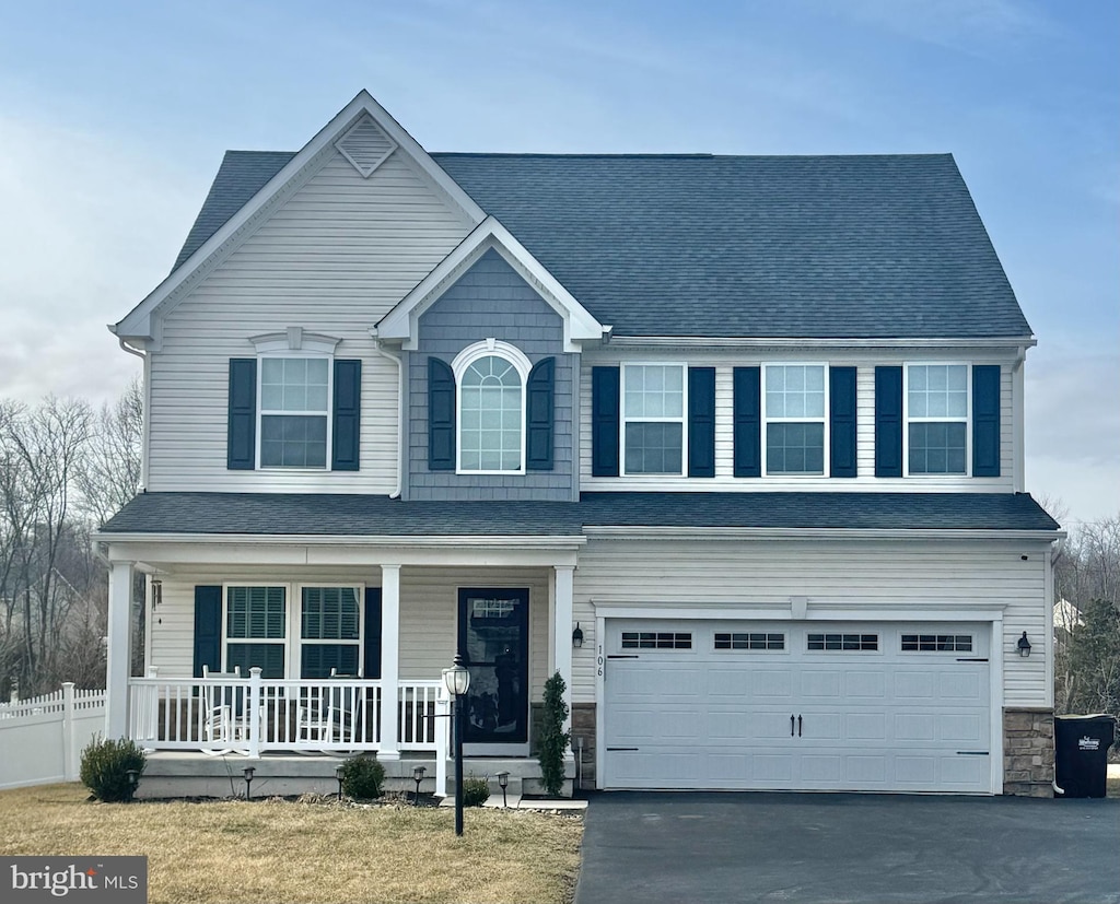 view of front facade featuring stone siding, covered porch, an attached garage, and fence