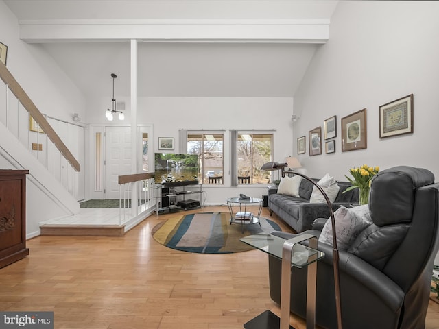 living room featuring beamed ceiling, stairway, light wood-type flooring, and high vaulted ceiling