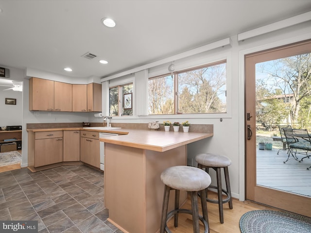 kitchen featuring dishwasher, a breakfast bar area, a peninsula, light brown cabinetry, and recessed lighting