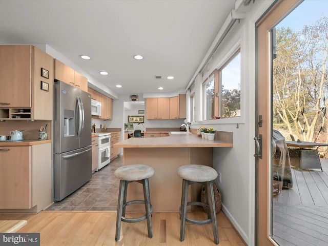 kitchen with a breakfast bar area, a peninsula, white appliances, light countertops, and light brown cabinetry